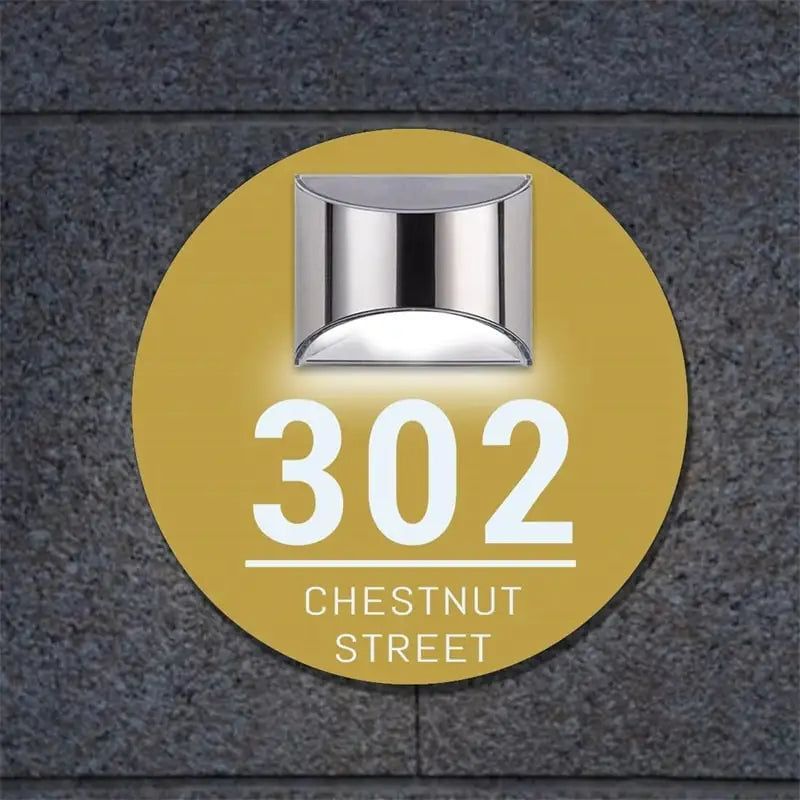 Round solar-powered acrylic house sign with custom engraved address number and street name mounted on wall